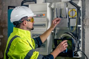Un technicien électricien travaillant dans un tableau de distribution avec fusibles. Installation et connexion des équipements électriques.